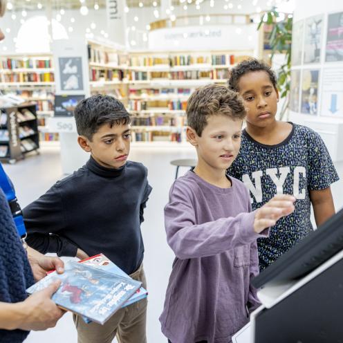 Tre børn og en bibliotekar foran udlånsautomat på biblioteket